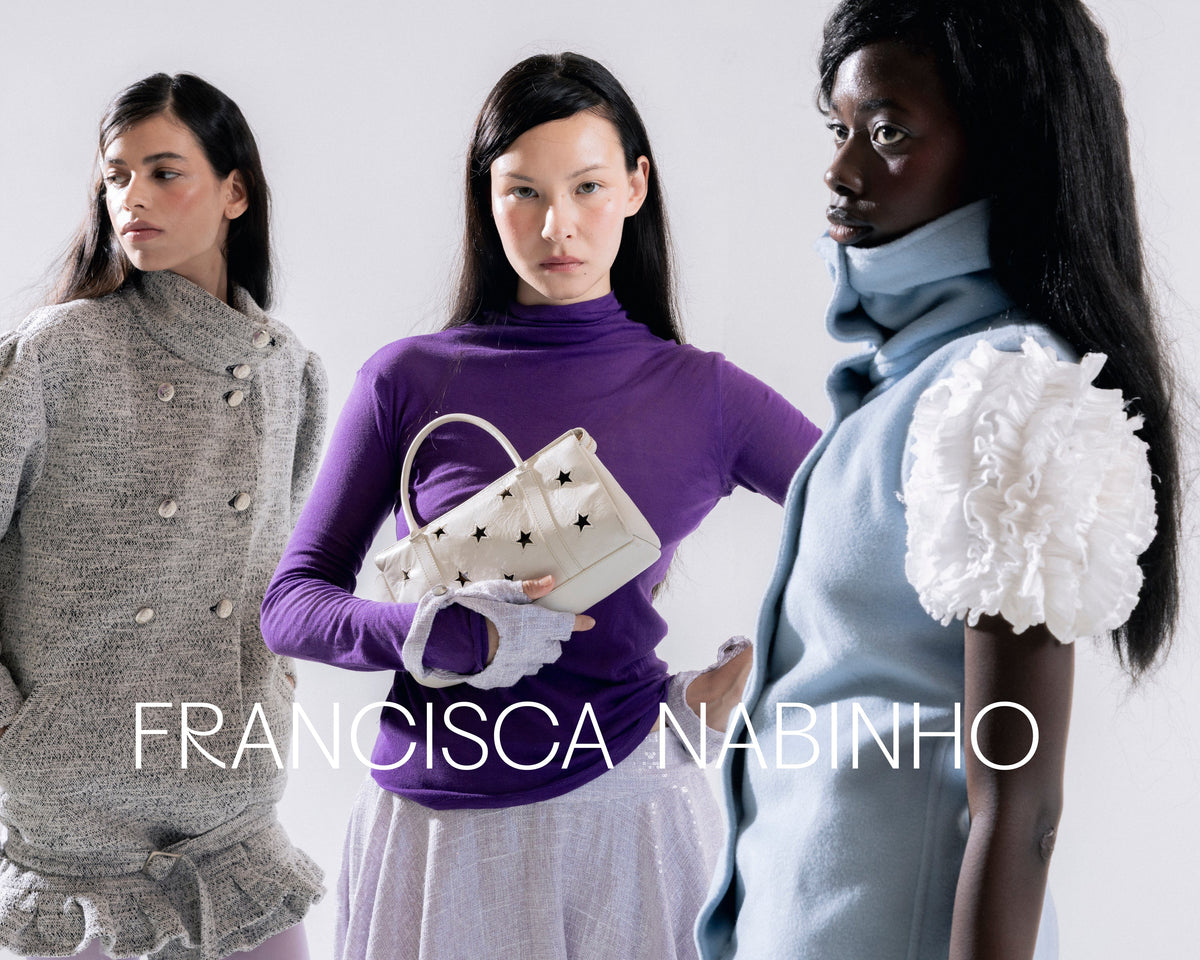 Three models pose in high-fashion clothing against a light gray studio background, with the text 'FRANCISCA NABINHO' overlaid at the bottom. The central model wears a purple turtleneck, white gloves, and holds a white handbag with black star details.